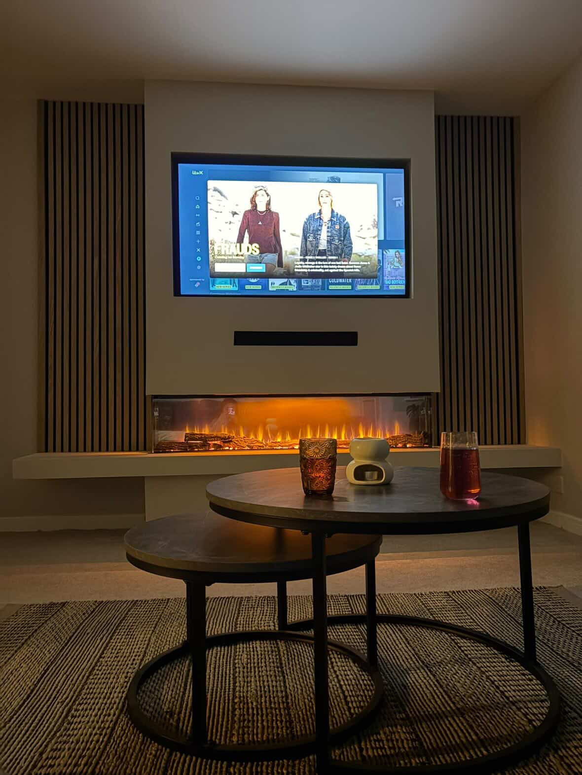 Symmetrical media wall with oak slat panels and a lit fire
