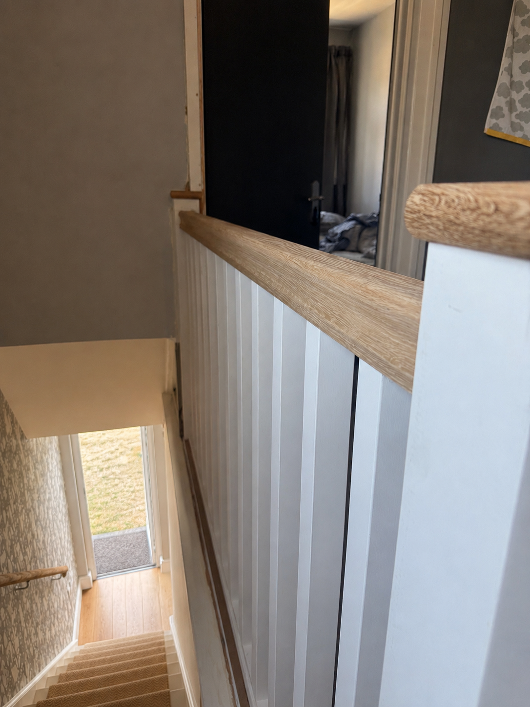 Oak handrail capping white tongue-and-groove panelling on a landing